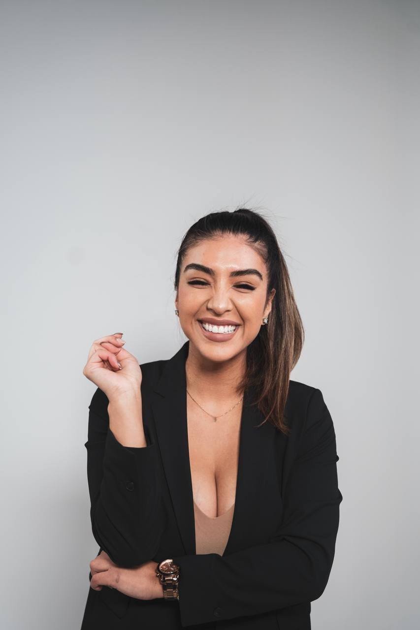 Cynthia smiling in a black blazer against a soft gray studio background.