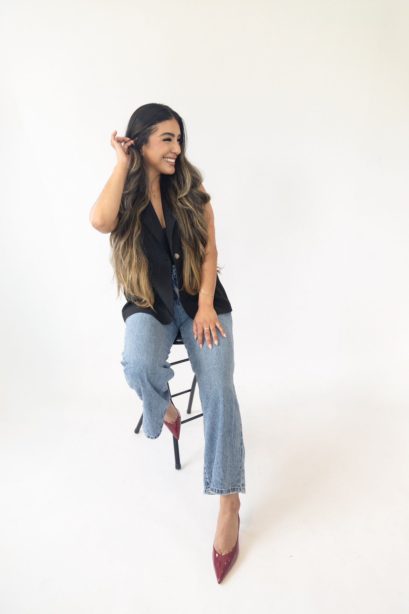 Cynthia seated on a tall stool in a black vest and blue jeans.