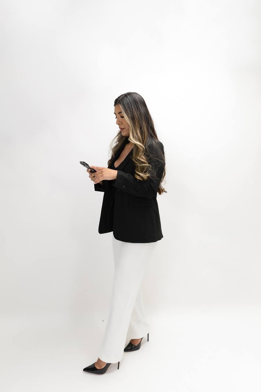 Cynthia standing in profile, wearing a black blazer and white trousers.